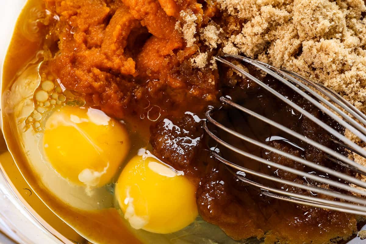 showing how to make pumpkin cupcakes by whisking the pumpkin puree, brown sugar, eggs, oil and vanilla together in a bowl