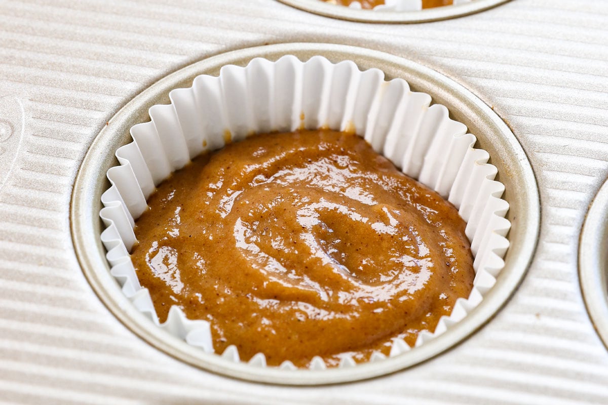 showing how to make pumpkin cupcakes by adding batter to cupcake liners