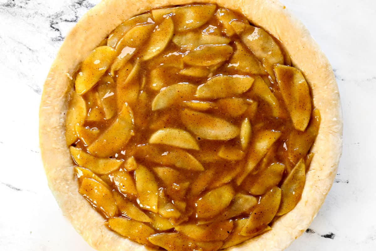 showing how to make homemade apple pie recipe by adding the apples to the pie crust in a pie plate