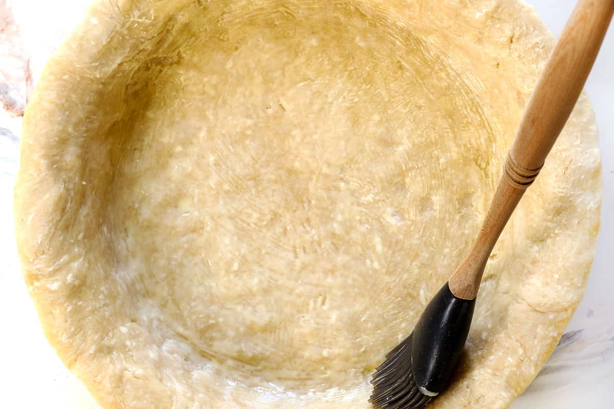 showing how to make traditional apple pie recipe by brushing the dough with an egg wash