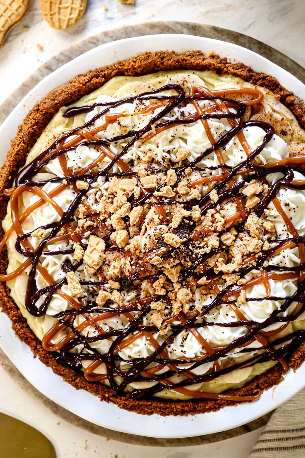 showing how to make banana cream pie by topping with whipped cream and drizzling with caramel sauce and chocolate