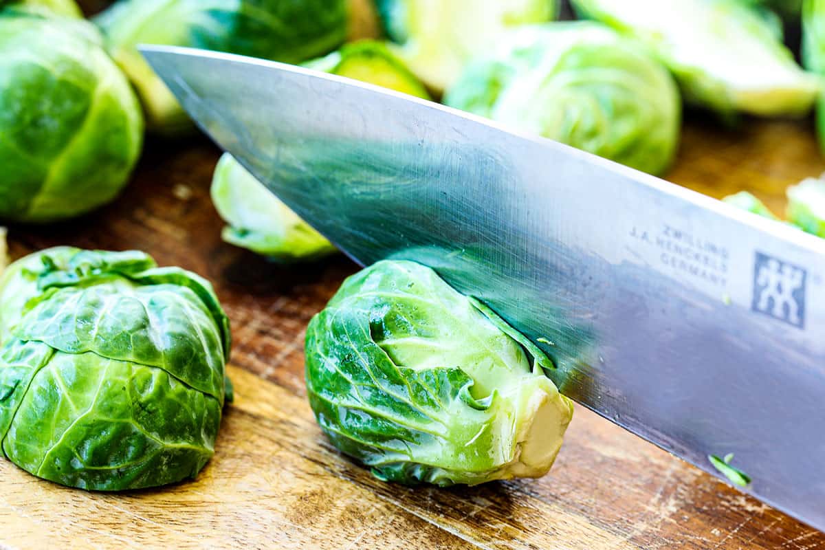 showing how to make Brussel sprouts with bacon by trimming the end off of the sprouts, then cutting them in halve