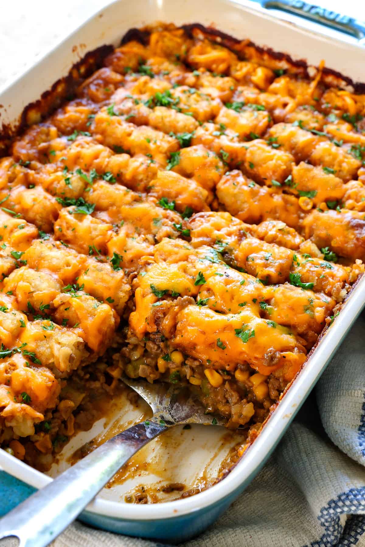 a serving spoon of best tater tot casserole with juicy ground beef, green beans, corn, and peas