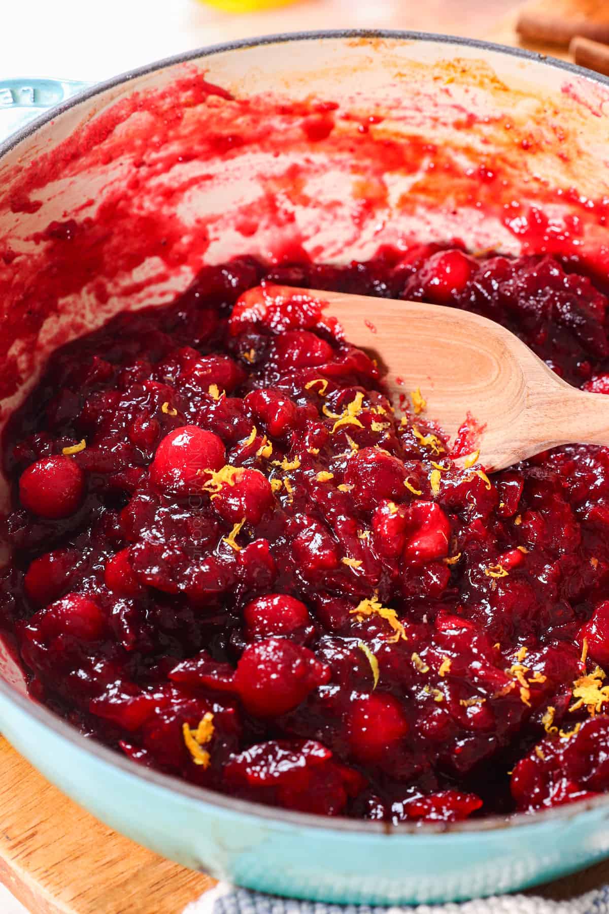 showing how to make cranberry sauce by stirring in the orange zest, whole cranberries and vanilla