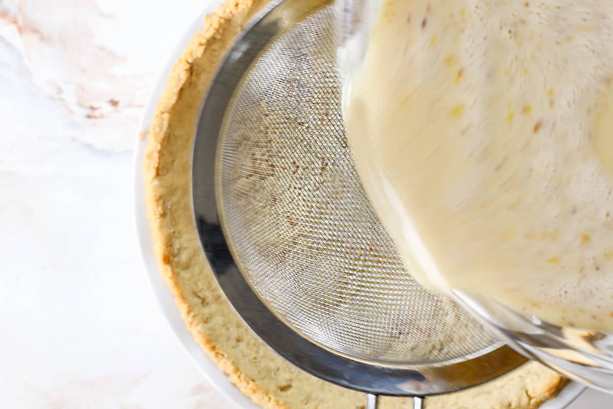 showing how to make custard pie by straining the custard through a fine mesh sieve in to the par-baked pie crust