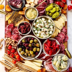 showing how to make antipasto by adding cheeses, meats, marinated vegetables, dried fruits and nuts on a platter