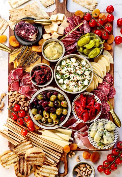 showing how to make antipasto by adding cheeses, meats, marinated vegetables, dried fruits and nuts on a platter