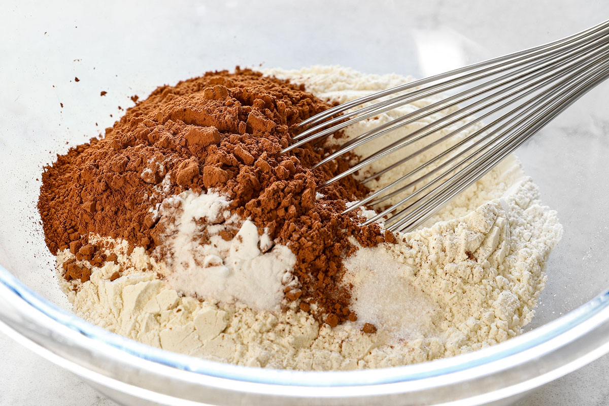 showing how to make red velvet cookies by whisking flour, cocoa powder, baking soda and salt together in a bowl.