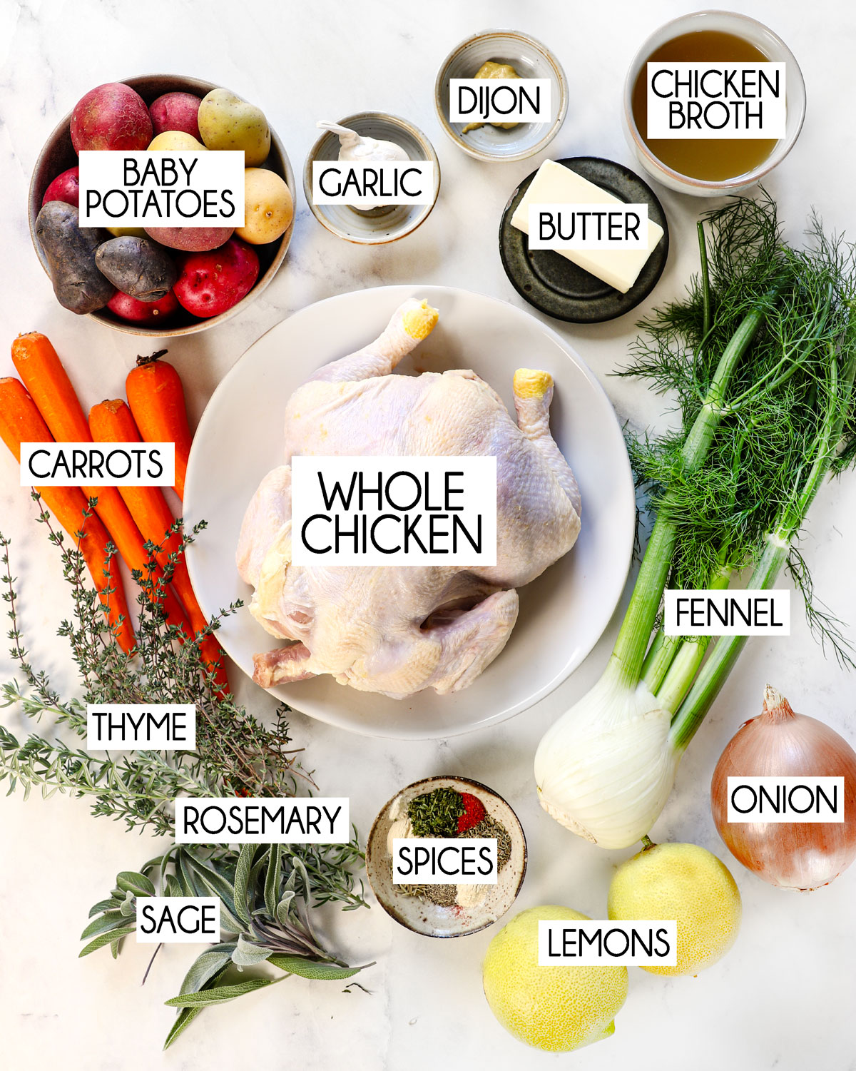 top view of roast chicken ingredients: whole chicken, garlic, onion, butter, rosemary, thyme, sage, butter, potatoes and carrots