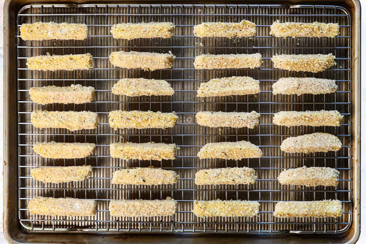 showing how to make mozzarella sticks by laying the breaded sticks onto a baking rack 