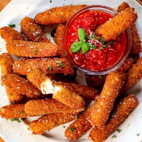 top view of serving mozzarella sticks on a platter with marinara with a cheese stick pulled apart showing the melty cheese