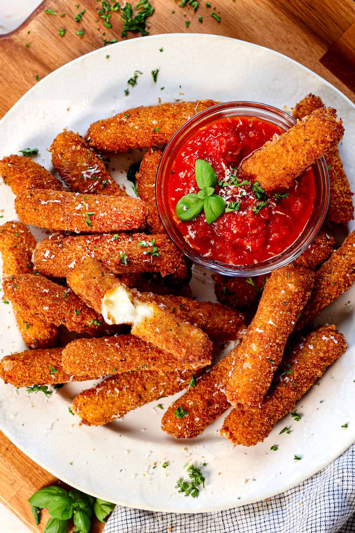 top view of serving mozzarella sticks on a platter with marinara with a cheese stick pulled apart showing the melty cheese