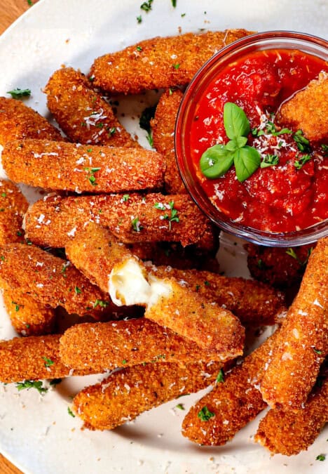 top view of serving mozzarella sticks on a platter with marinara with a cheese stick pulled apart showing the melty cheese