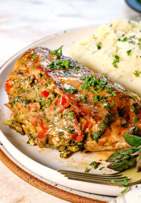 up close of serving baked stuffed chicken breast on a plate with mashed potatoes and asparagus