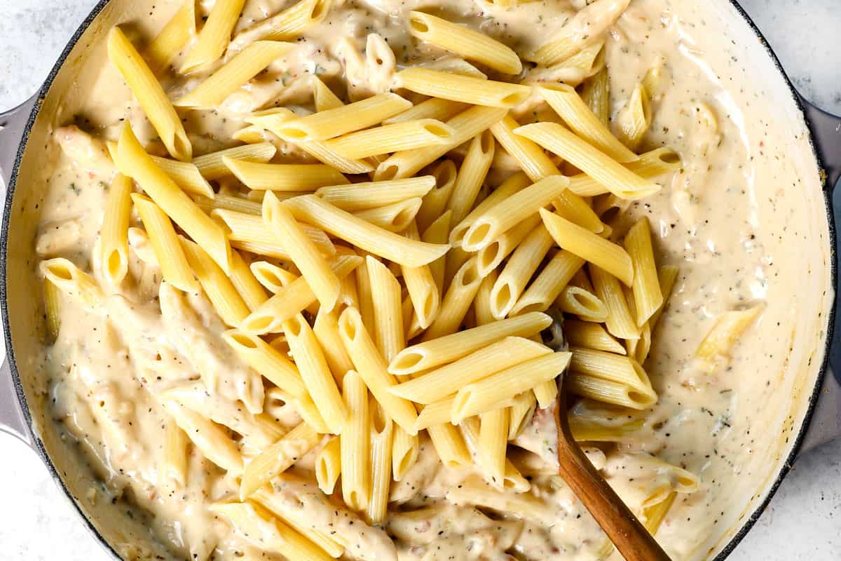 showing how to make Chicken Parmesan pasta by stirring in the penne pasta