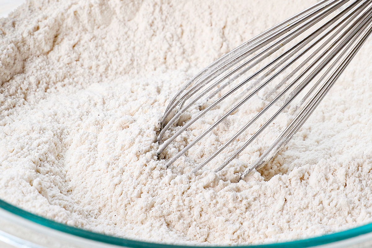 showing how to make fluffy pancakes recipe by whisking the flour, sugar, baking powder, cinnamon, and salt in a large mixing bowl.