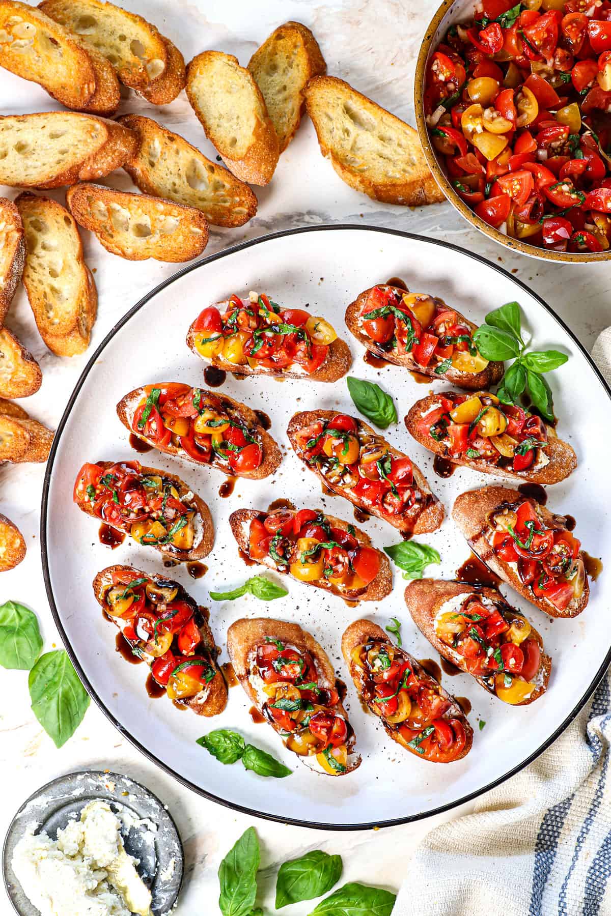 Italian bruschetta recipe surrounded by toasts, basil and goat cheese on a platter