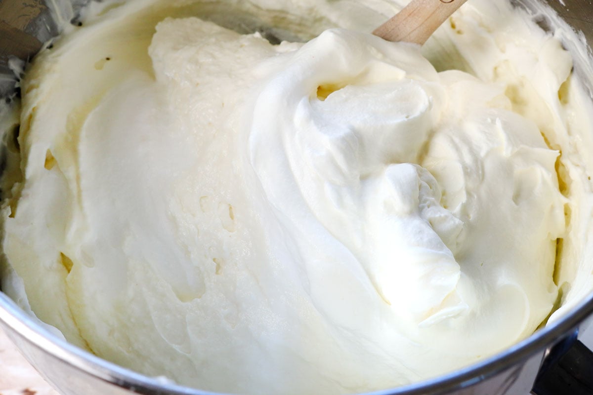 showing how to make no bake cheesecake recipe by folding the whipped cream into the cream cheese mixture