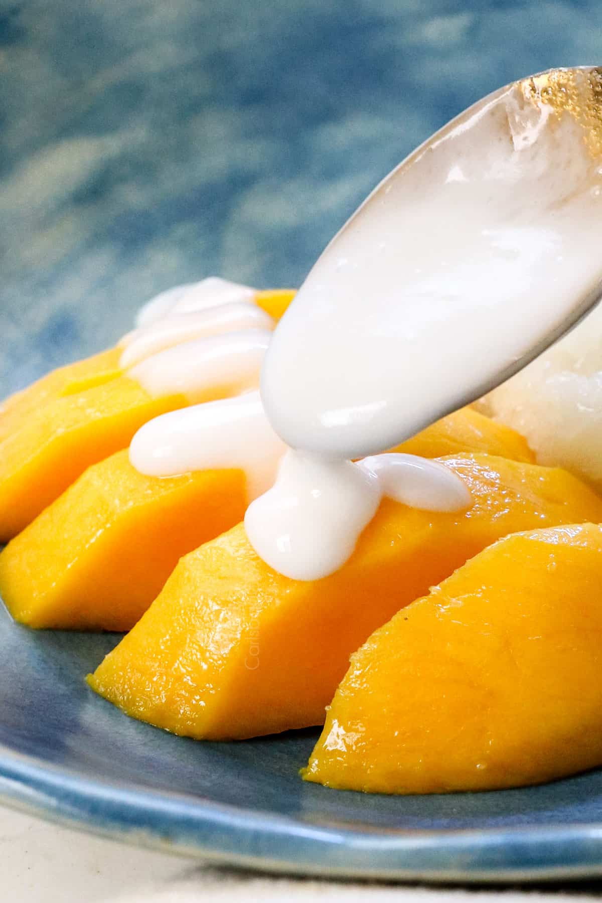 showing how to make mango sticky rice by spooning the coconut sauce over the mango and sticky rice