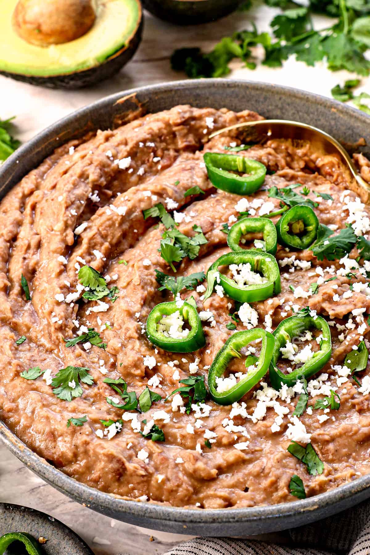 side view of homemade refried beans topped with jalapeno slices and cotija cheese showing the creamy texture