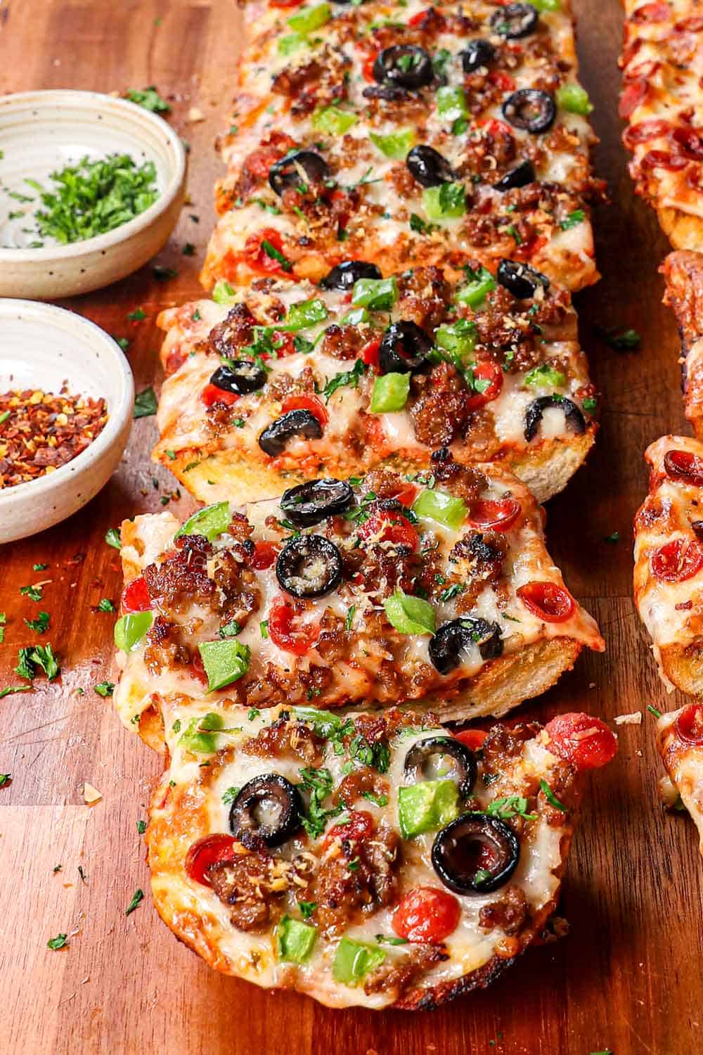 pizza bread with pepperoni and sausage with pizza sauce sliced on a cutting board