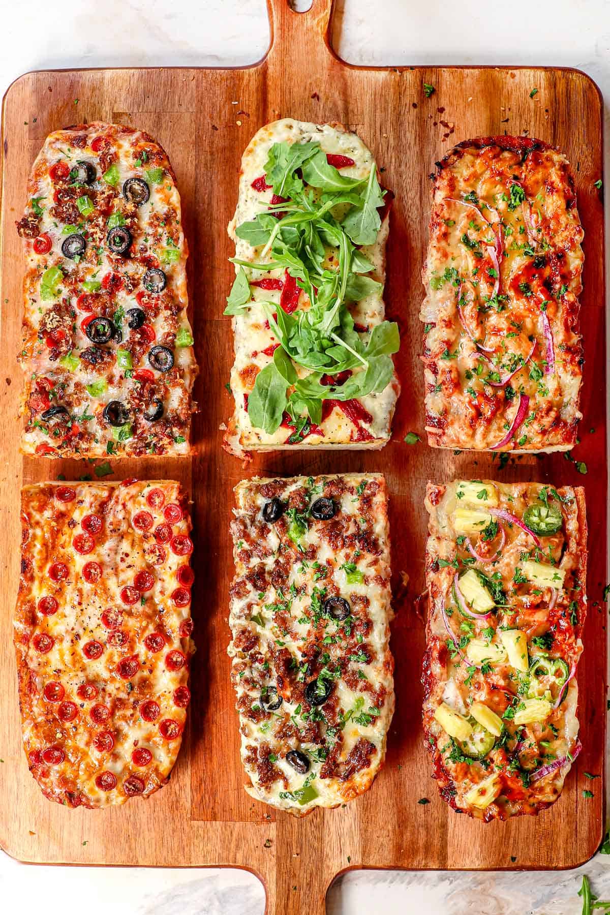 top view of homemade french bread pizza on a cutting board with three different variations (classic with pepperoni, and classic supreme, barbecue chicken pizza and white pizza)