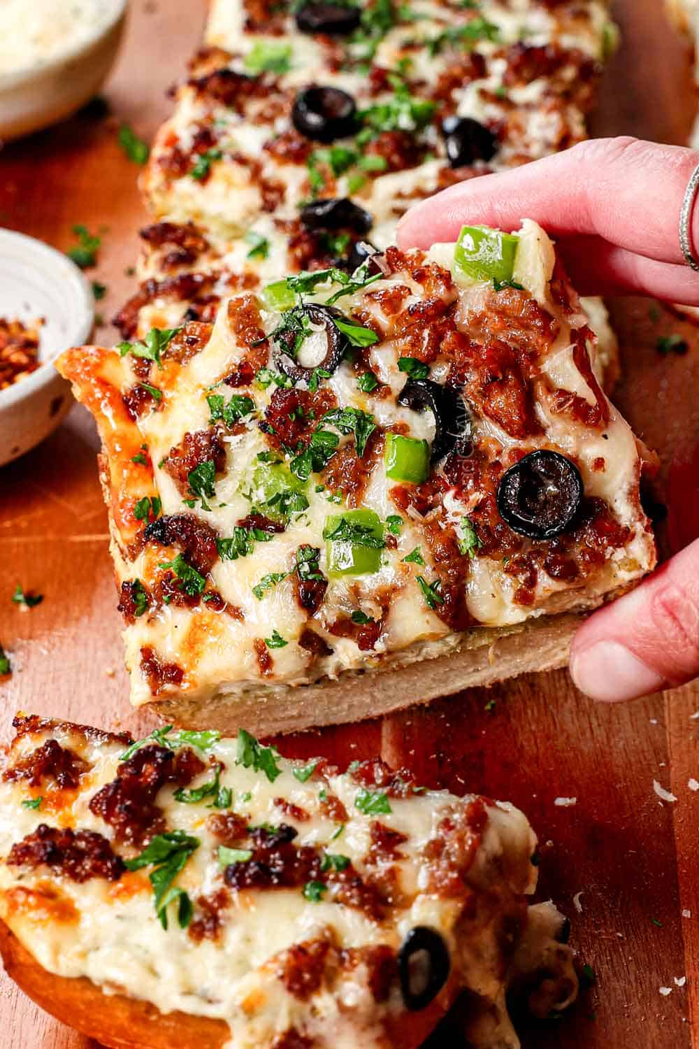 picking up a slice of French bread pizza showing the toppings, cheese, and crispy crust