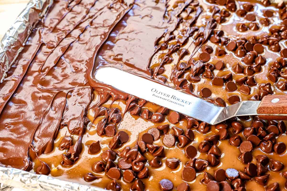 showing how to make almond roca by spreading the melty chocolate chips over the toffee