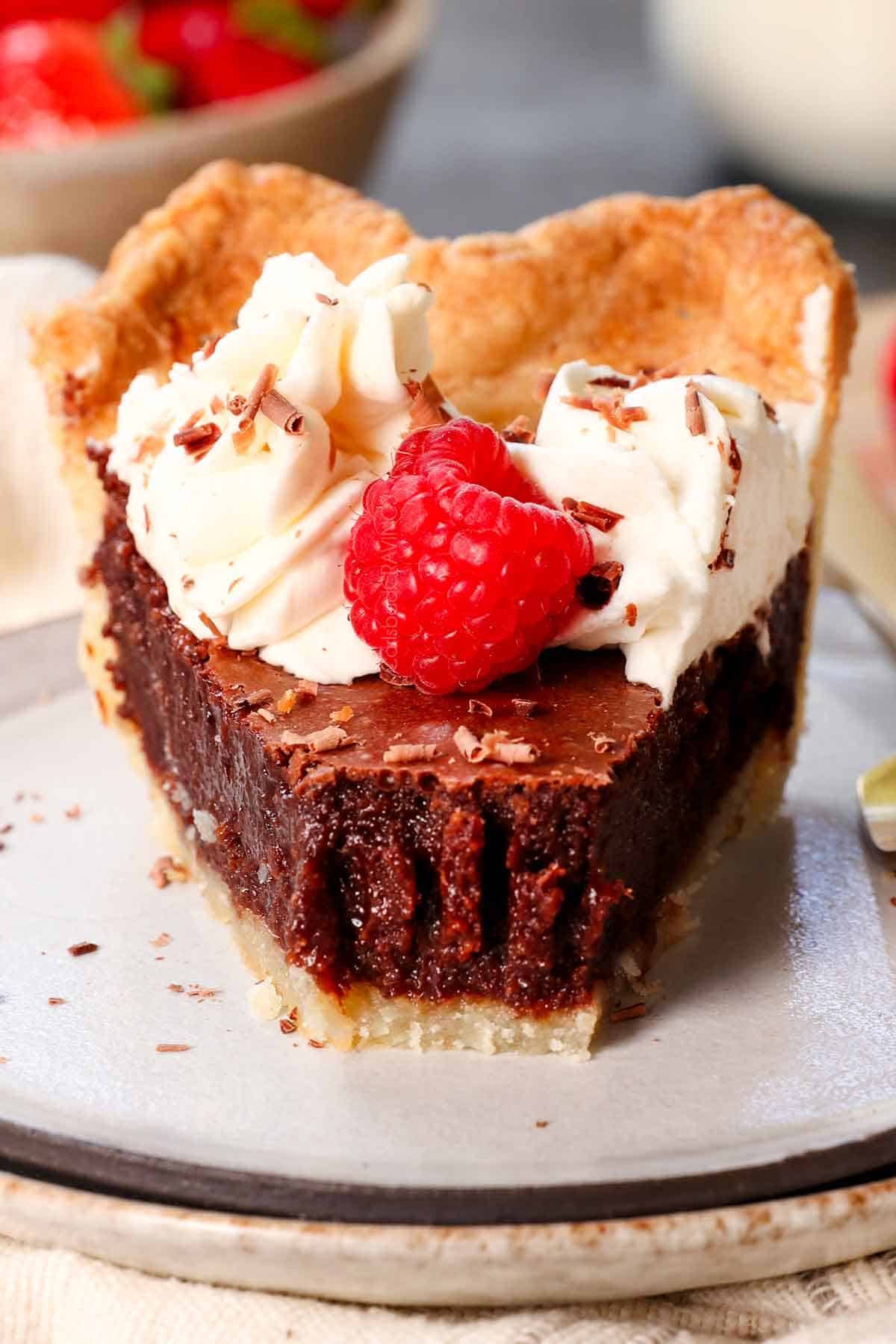 up close of a slice of chocolate chess pie with a bite taken out, garnished by whipped cream and raspberries