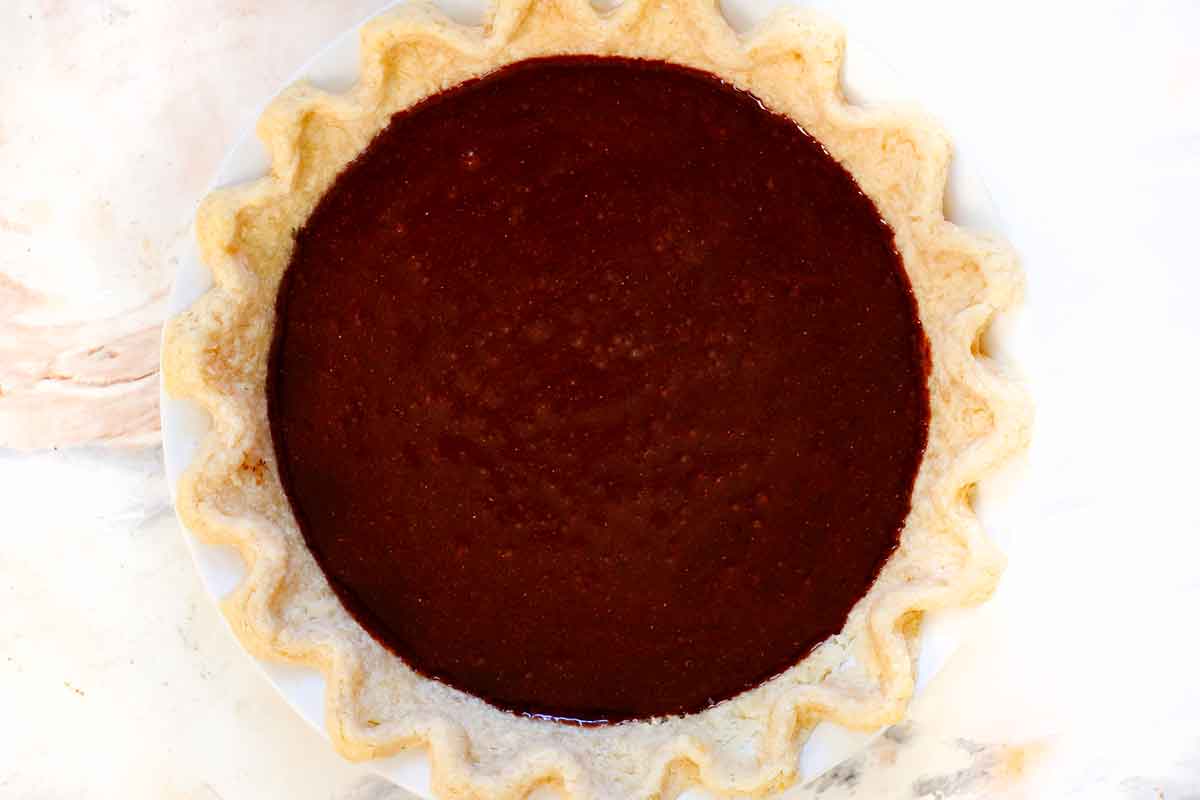 showing how to make chocolate chess pie by adding the filling to the par baked pie crust and baking