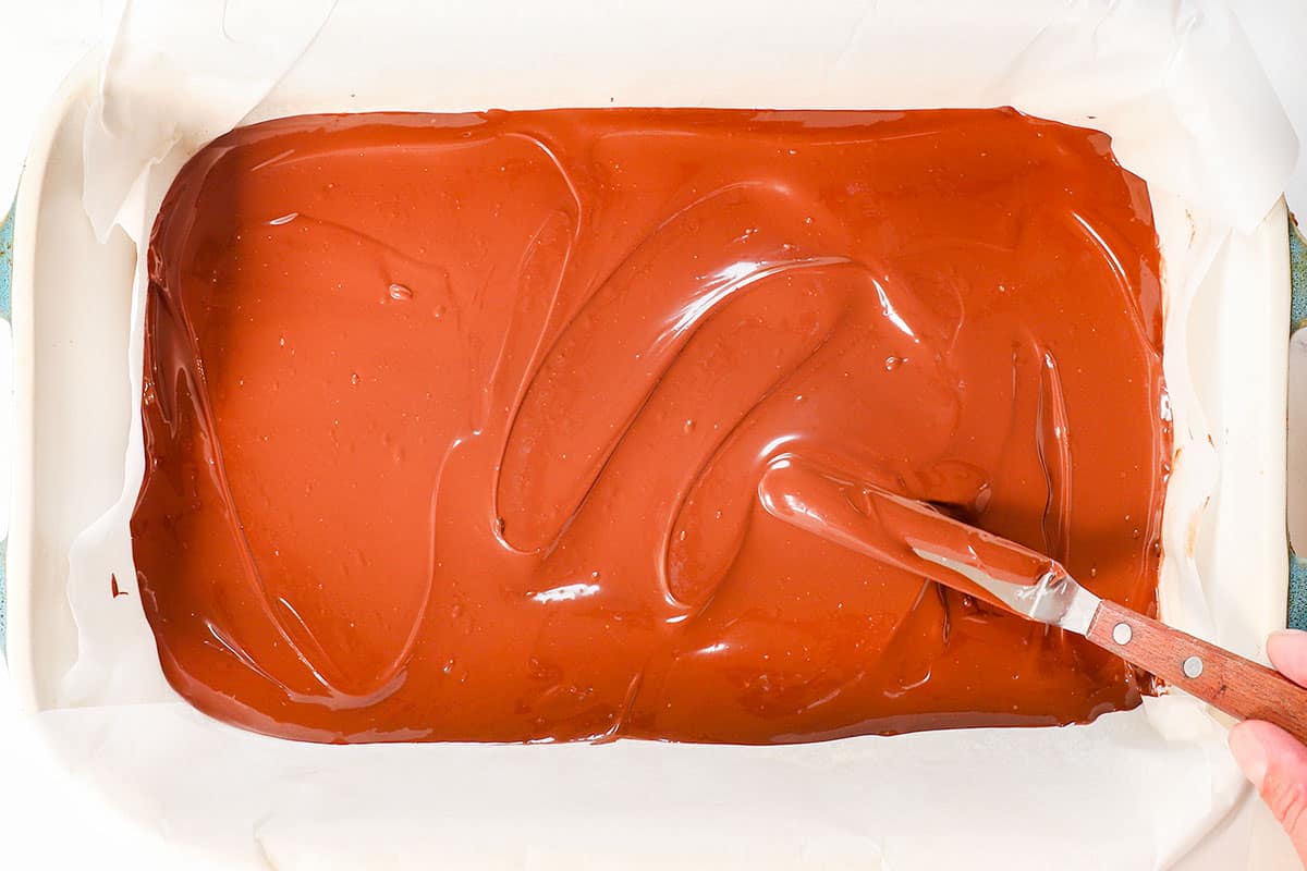 showing how to make peppermint bark by spreading the chocolate in the bottom of a 9x13 parchment paper lined baking dish