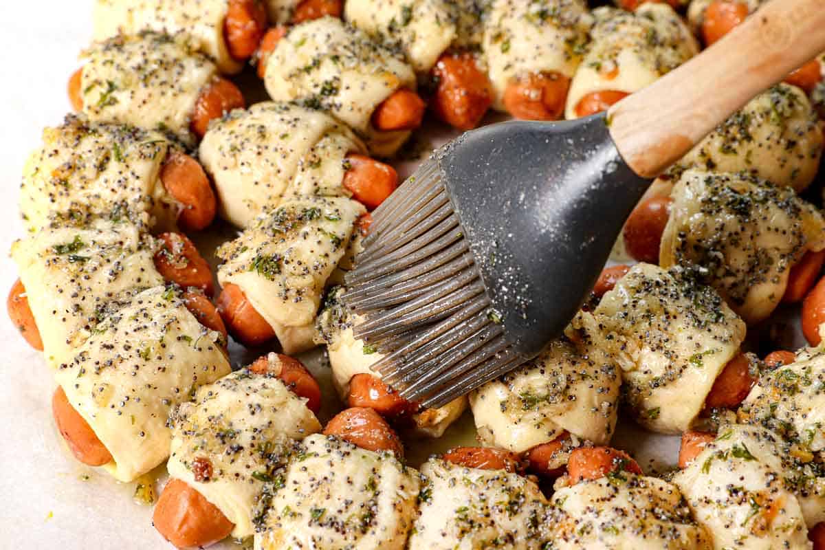 showing how to make pigs in a blanket with crescent rolls by brushing the rolls with poppy seed butter