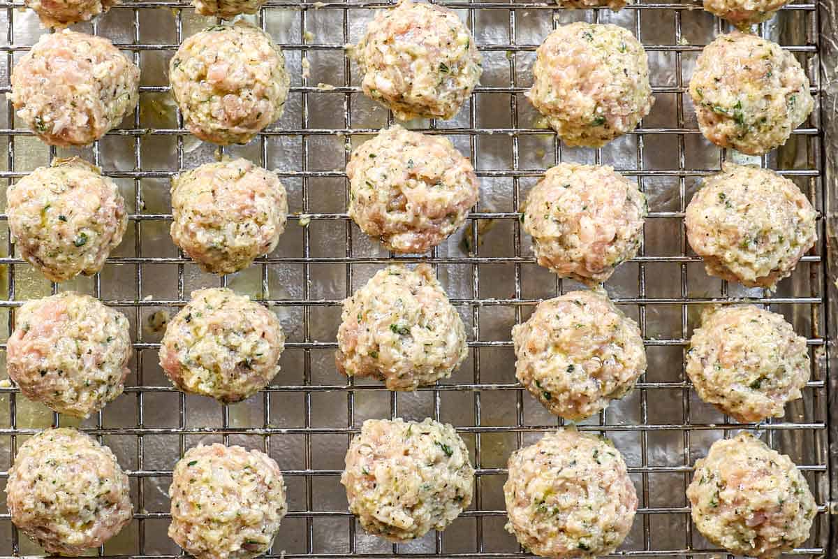 showing how to make chicken meatballs by scooping the mixture by the 1 ½ tablespoon, then rolling into balls and placing on a baking rack