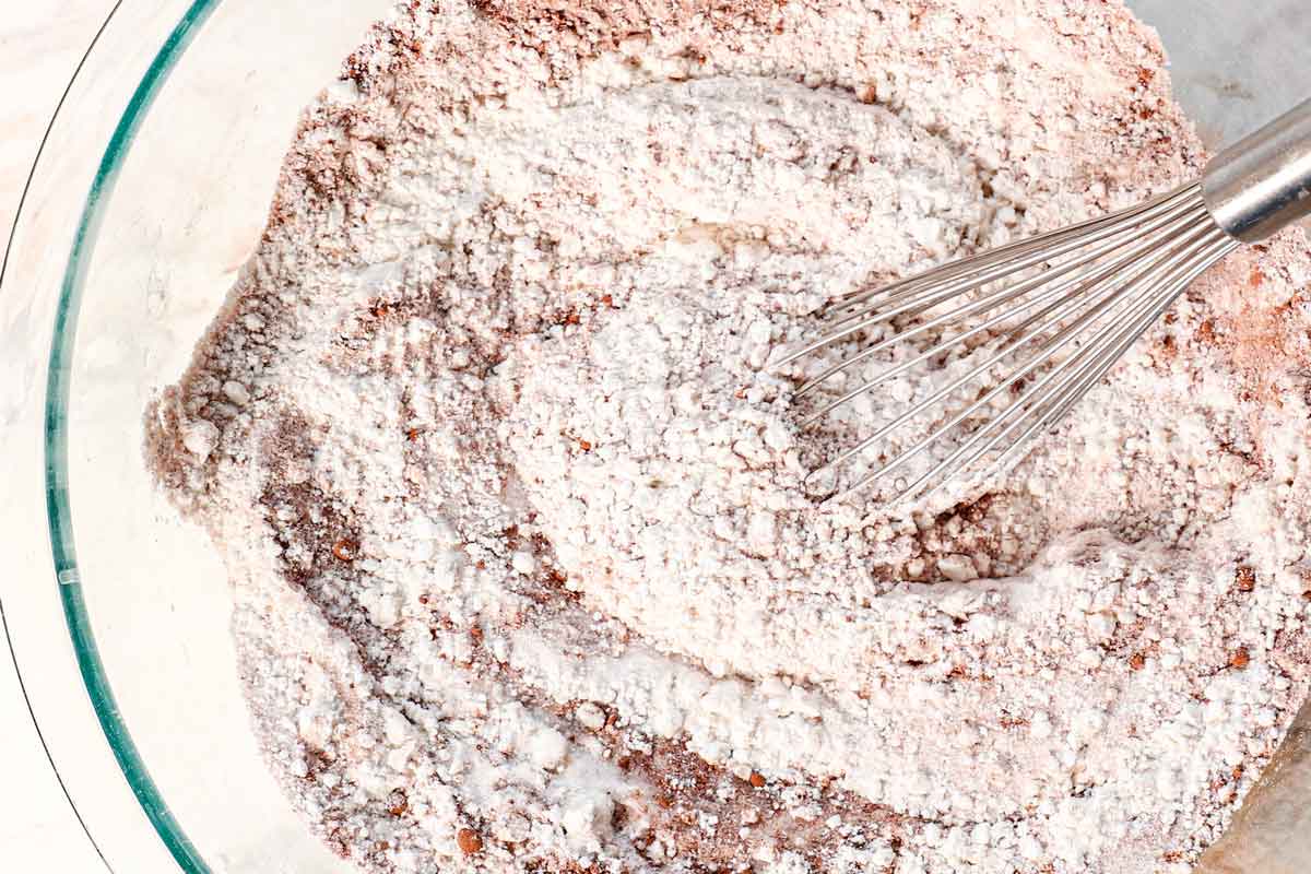 showing how to make red velvet cake by whisking together the flour, cocoa powder, baking soda, and salt
