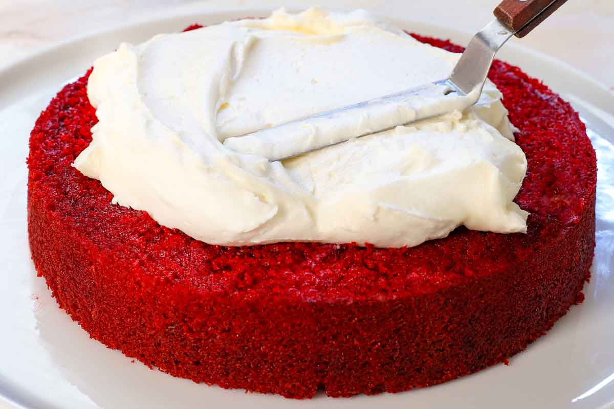showing how to make red velvet cake by adding a layer of frosting to the first cake layer