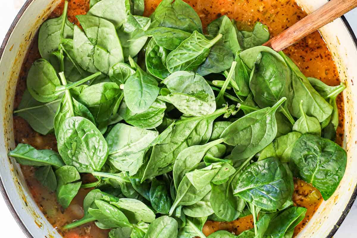 showing how to make white bean soup by adding the evaporated milk to make it creamy and the kale or spinach