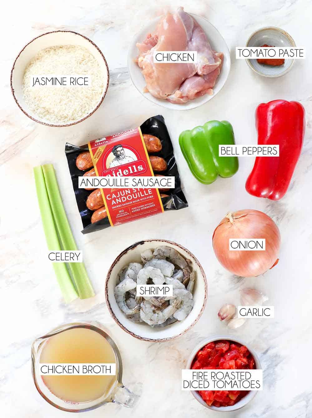 top view of Jambalaya ingredients: andouille sausage, chicken, shrimp, onions, bell peppers, celery, tomatoes, chicken broth, garlic, Cajun seasoning, rice, chicken broth