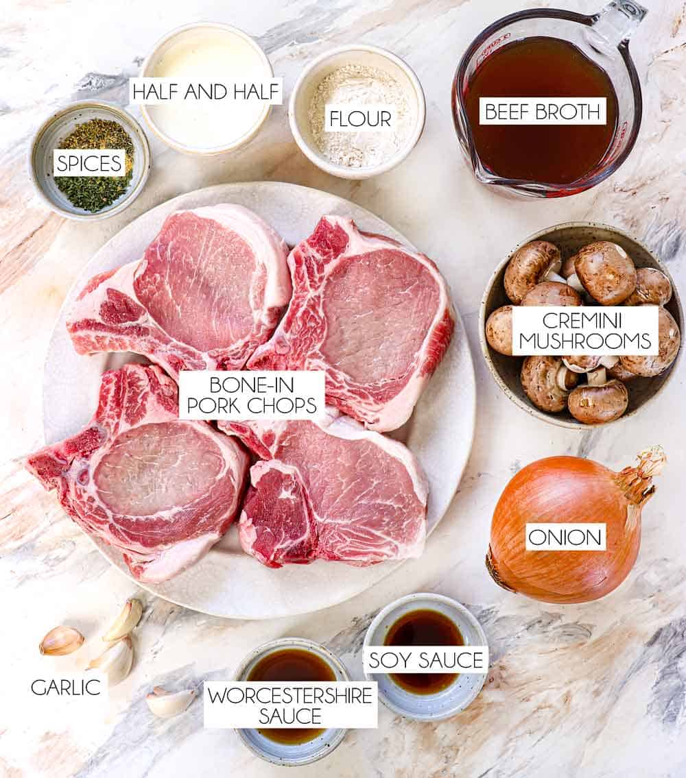 top view of smothered pork chops ingredients: bone in pork, cremini mushrooms, onions, beef broth, half and half, spices, flour, garlic, Worcestershire sauce