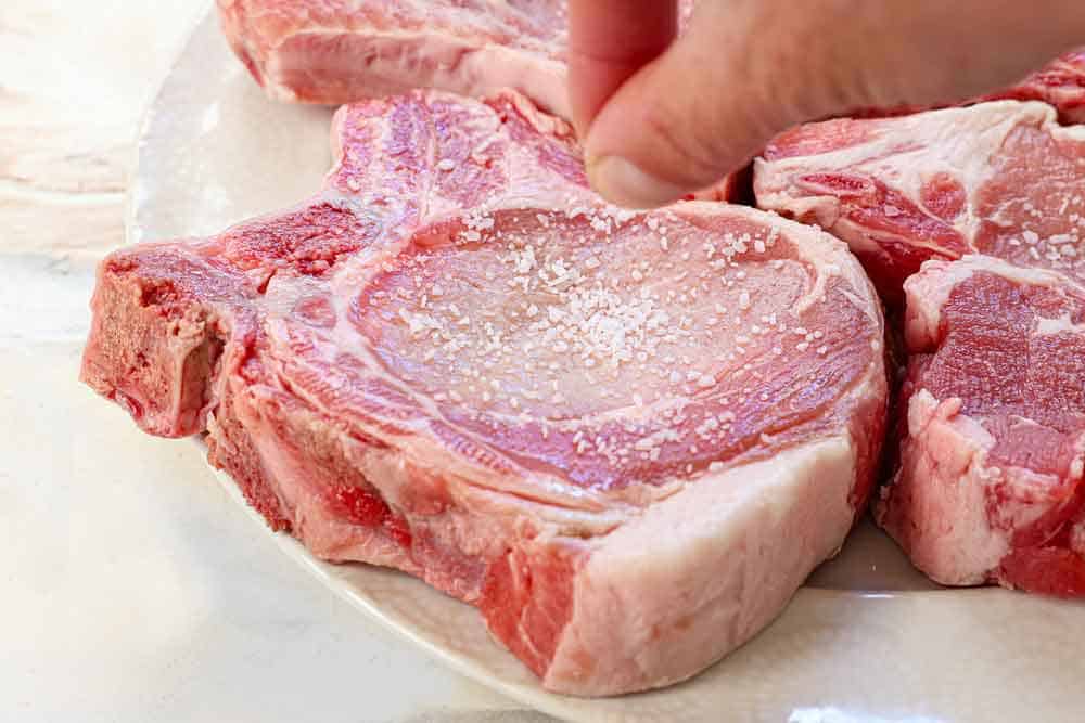 showing how to make smothered pork chops by sprinkling with kosher salt to dry brine