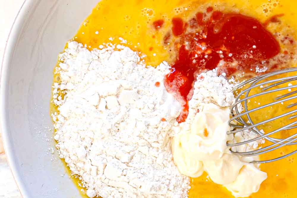 showing how to make hot honey chicken by whisking together eggs, flour, hot sauce and mayonnaise to make a batter