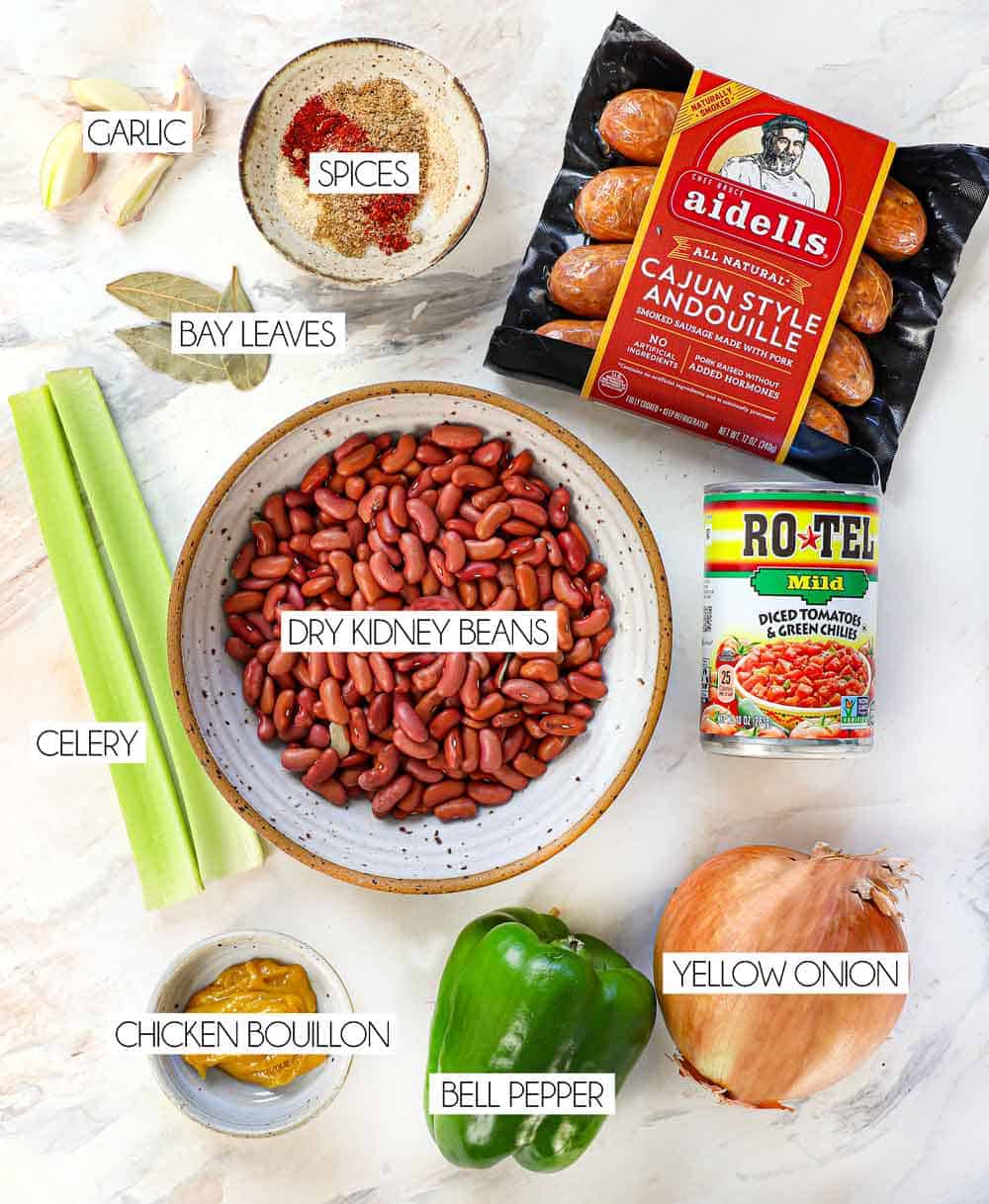 top view of red beans and rice recipe ingredients: dry kidney beans, andouille sausage, celery, onion, bell pepper, garlic, Cajun spices, bay leaves, tomatoes