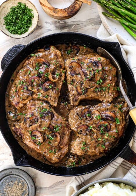 showing how to make smothered pork chops by resting in the sauce
