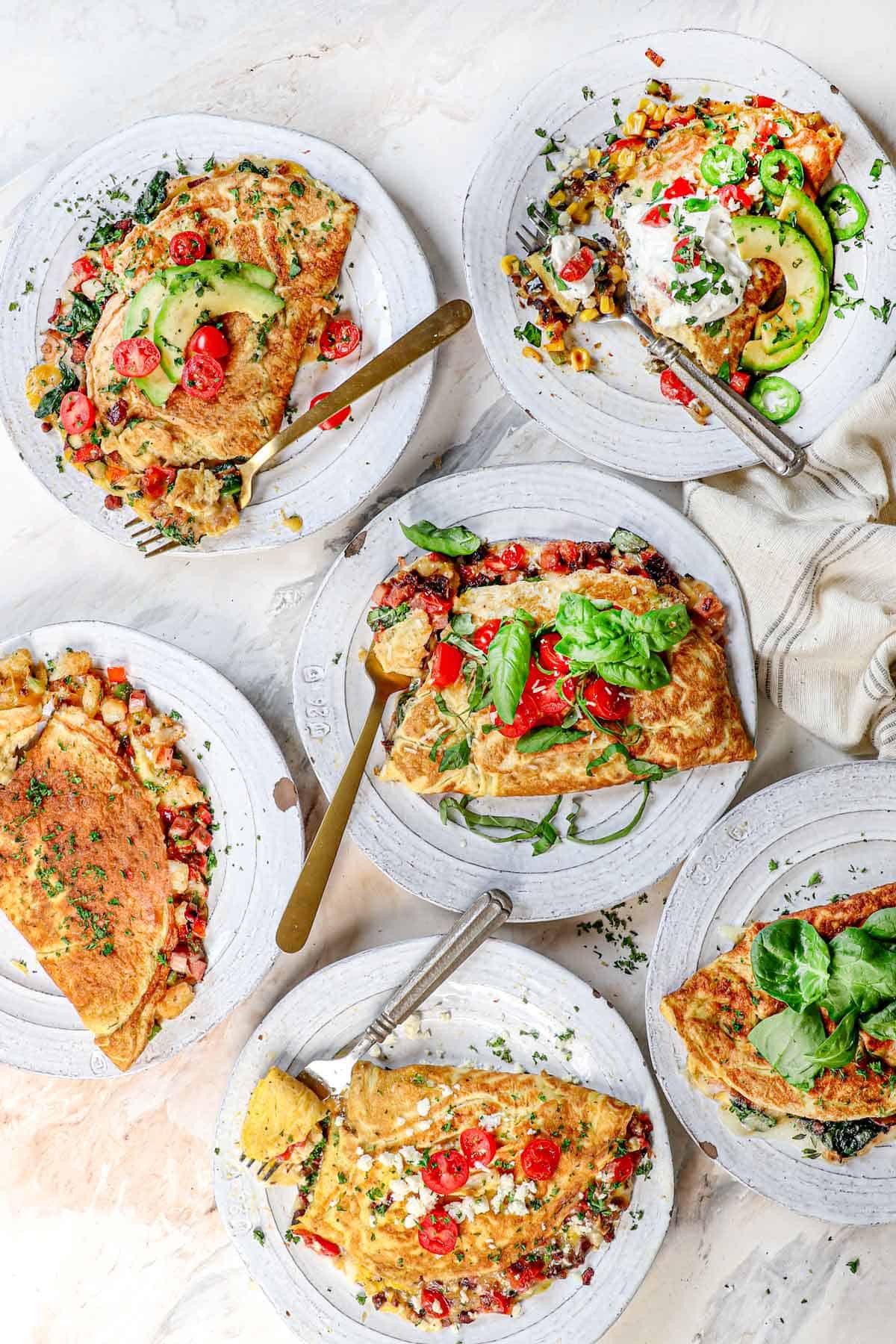 top view of 8 variations of omelette recipe: Denver omelette, Spinach omelette, Greek omelette, California omelette, veggie omelette, Italian omelette, breakfast omelette, Mexican omelette