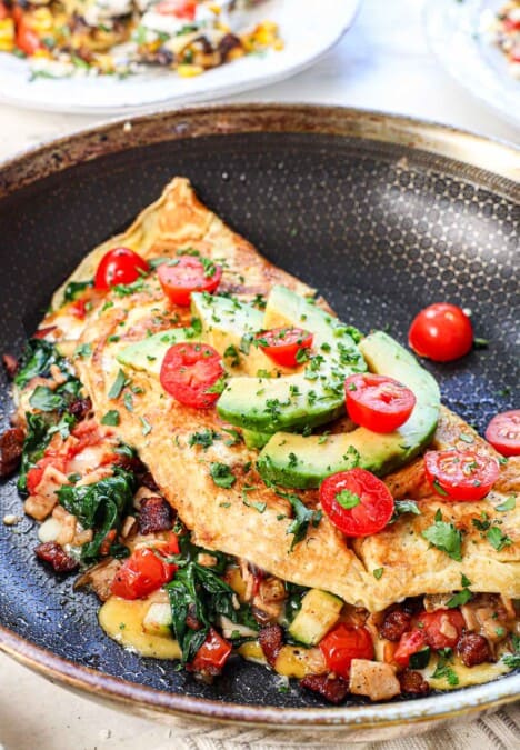 omelet in a skillet garnished with tomatoes, avocado and parsley, showing how to serve