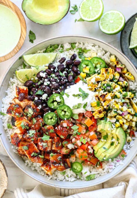 showing how to make chipotle honey chicken by adding the chicken to rice with beans, corn, pico e gallo, avocados, and cilantro