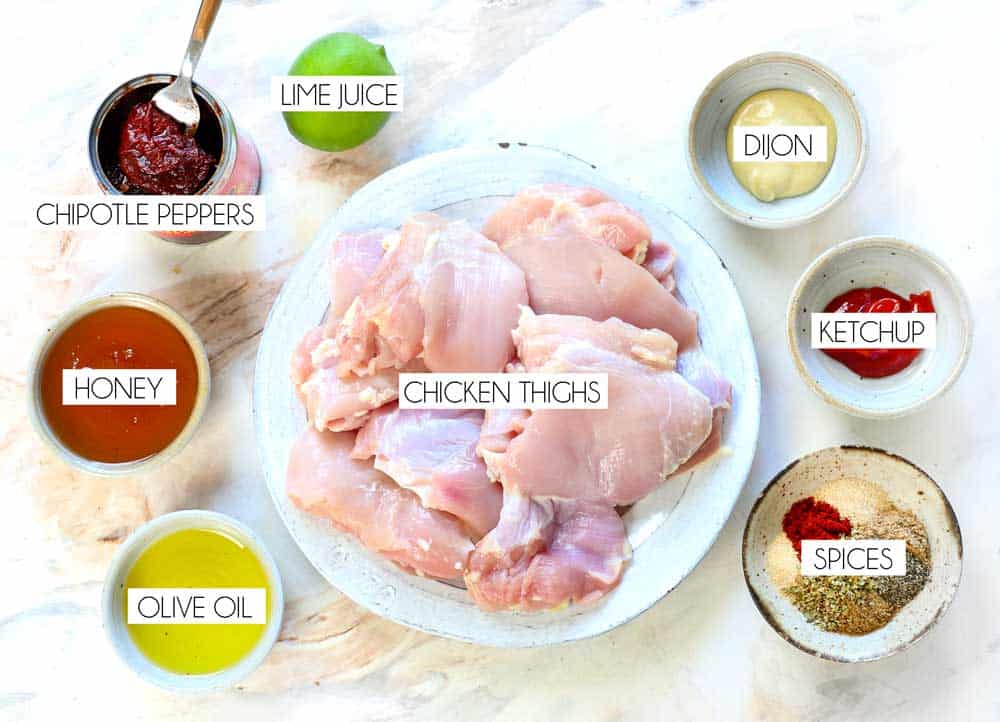 top view of chipotle honey chicken ingredients: chicken thighs, honey, chipotle peppers, lime juice, Dijon, ketchup, olive oil, spices
