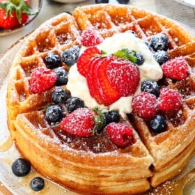 Belgian waffles stacked on a plate showing how fluffy they are, served with syrup, whipped cream, and berries
