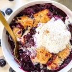 top up close view of a bowl of blueberry cobbler showing the biscuit topping and juicy berries served with vanilla ice cream