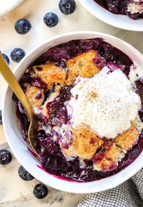 top up close view of a bowl of blueberry cobbler showing the biscuit topping and juicy berries served with vanilla ice cream