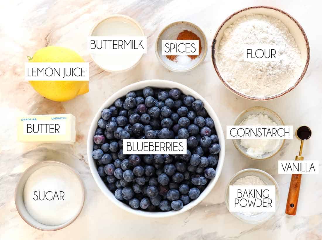 top view of blueberry cobbler ingredients: blueberries, flour, sugar, baking powder, cinnamon, cornstarch, buttermilk, cinnamon, lemon juice